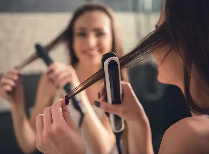 笑顔でヘアアイロンをかける女性